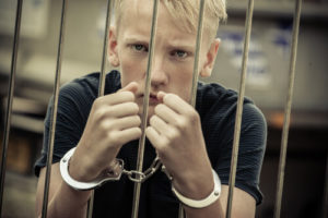 Disgruntled White Juvenile Male Handcuffed Behind Jail Cell Bars