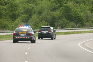 Police Car With Lights On Closely Pursuing A Black Minivan On A Two Lane Road