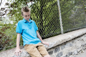 Young White Boy Sitting On Low Stone Barrier