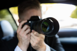 White Male Sitting In A Vehicle Taking A Picture With A DSLR Equipped With A Telephoto Lens