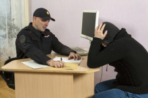 Police Officer Seated At Desk Questioning Seated Suspect