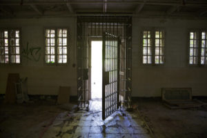 Light Shining Through Barred Door Partly Open In The Middle Of A Dark Rundown Room