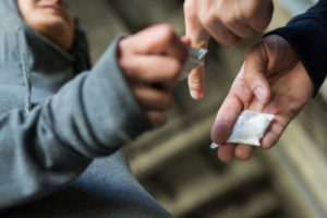 Man In Gray Hoodie Handing Money to Person Holding A Small Bag Filled With A White Substance