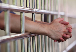 White Male With Arms And Hands Clasped Placed Through Jail Cell Bars